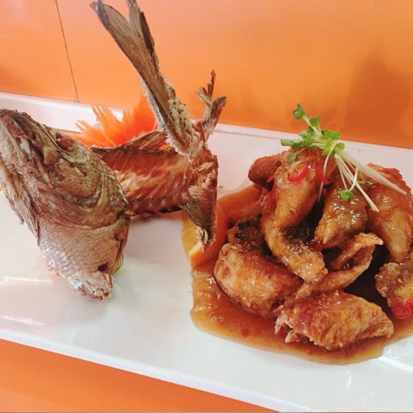 Fried fish head and tail with crispy fish pieces in sauce, garnished with sprouts and chili.