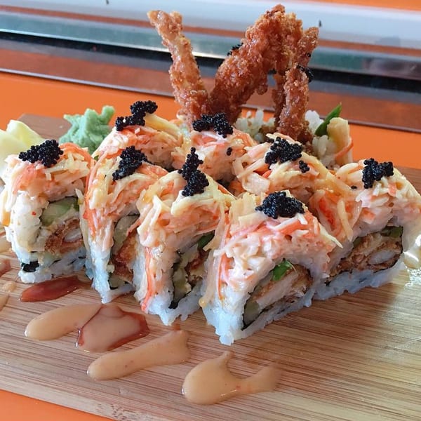 J-Dao Sushi Thai's sushi rolls with crab, avocado, fried shrimp, and black caviar on a wooden board.
