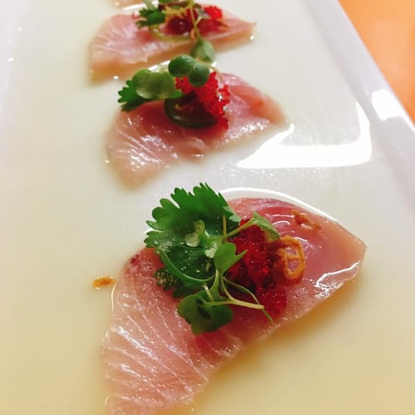 Three pieces of J-Dao Sushi Thai sashimi with red roe and green herbs on a white plate.